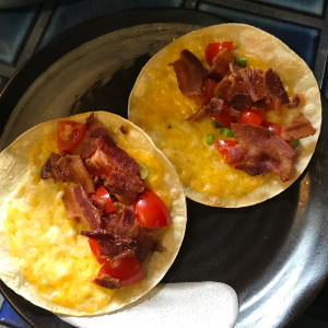 A top down photo of 2 tacos stuffed with tomatoes, scallions and bacon