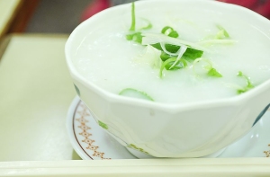 A photo of a bowl of congee with scallions sitting on a table