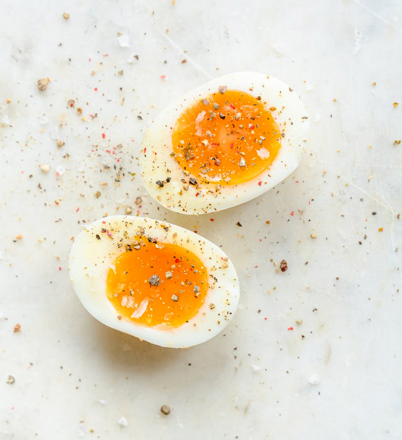 A photo of boiled eggs sliced in half with ground pink peppercorns and kosher salt sprinkled over them on a white background