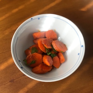 A top down photo of a white bowl with carrot salad in it on a wooden table. 
