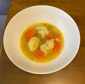 A photo of a bowl of soup containing three dumplings