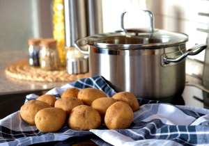 A photo of raw potatoes on a table near a cooking pot. 