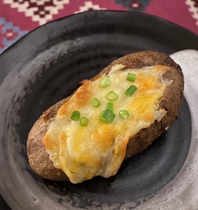 A baked potato topped with melted cheese and scallions