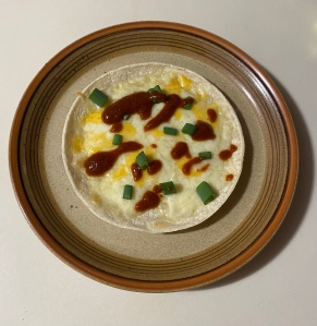A corn tortilla topped with melted cheese, scallions and taco sauce. 