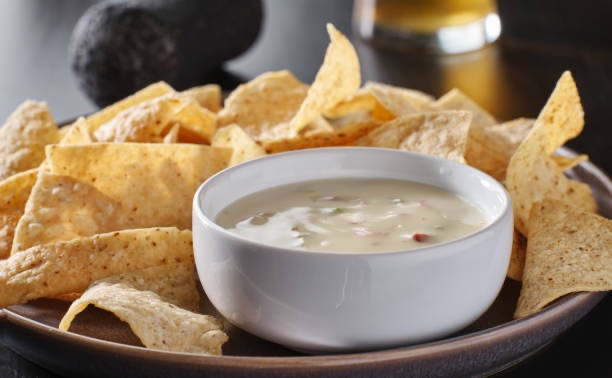A bowl of queso surrounded by tortilla chips