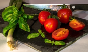 A cutting board with basil, tomatoes and scallions