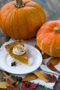 Pumpkins, a slice of pumpkin pie, spices and fall leaves sitting on a table. 