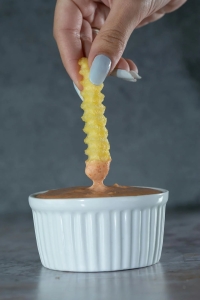 A single French fry being dipped in sauce